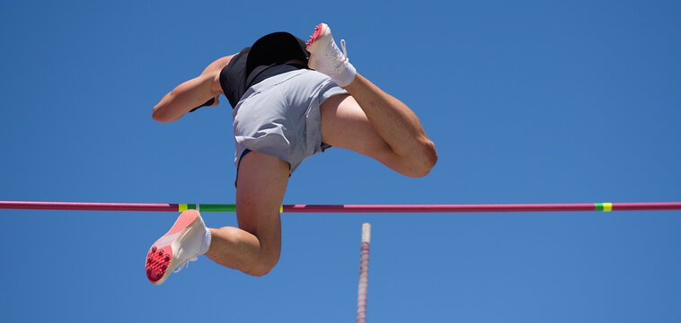 Athlete pole vault with a blue sky. Polevaulter pulling herself over the pole vault crossbar