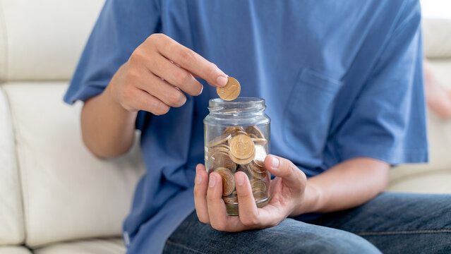 Man Putting Indonesian Rupiah Coins into Glass Jar for Savings