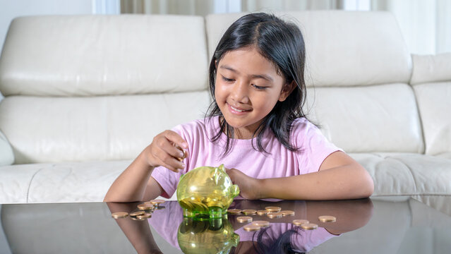 Smiling Young Asian Girl Putting Coins into a Piggy Bank to Save Money