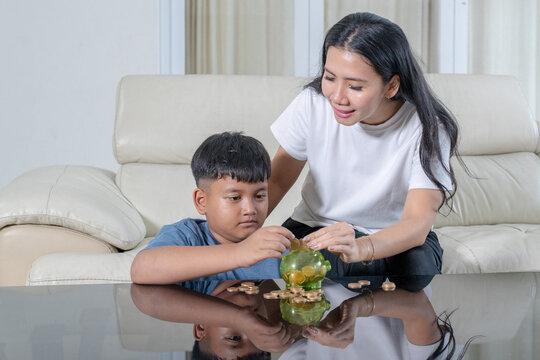 Asian Mother Helping Her Young Son Save Money with Piggy Bank at Home