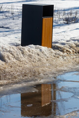 Fototapeta premium Black and wood trash bin stands in snowy field
