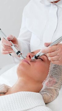 Middle-aged girl lies relaxed during lips zone rejuvenation with microcurrent device. Young adult woman gets facial procedure from cosmetologist in beauty clinic, enhancing skin tone and freshness