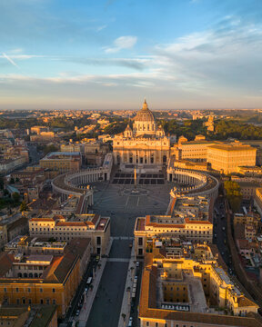 Aerial view of St. Peter's Basilica and St. Peter's Square at sunset, with golden light illuminating the historic architecture and surrounding urban landscape in Rome, Lazio, Italy.
