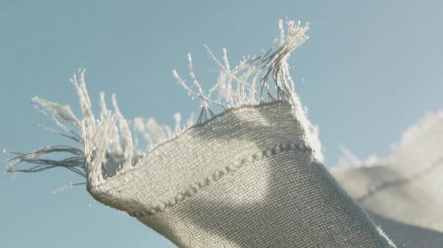 Lifting light woven cloth fringe by breeze under pale blue sky, seam and threads catching sun
