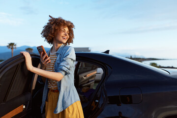 Naklejka premium Cheerful woman outdoors, smiling near a car, wearing a denim jacket over a striped top and a yellow dress, enjoying a sunny, relaxed lifestyle moment