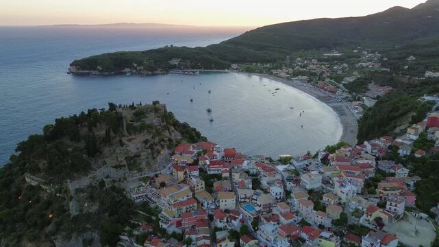 Cinematic drone view descending from high altitude to reveal a beautiful coastal resort town next to a large sandy beach bay during twilight.