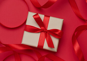 Fototapeta premium Gift box in beige packaging with red satin bow on a red background