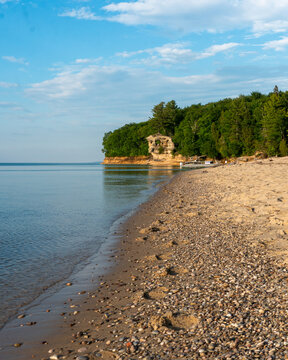 Aerial view of Chapel Rock at Pictured Rocks National Lakeshore with a sandy beach, calm water, and dense forest in Michigan, United States.