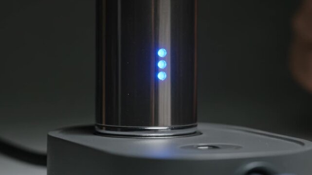 Positioning operator hands guiding metal cylinder into matte base at tabletop, activating blue LEDs