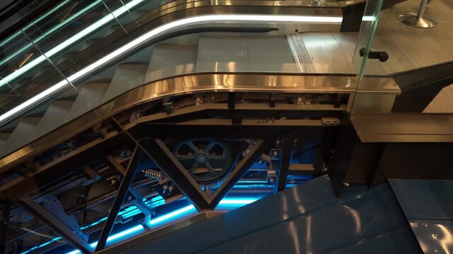 Escalator mechanism operates inside public building. Exposed internal gears, chains and drive wheel show mechanical engineering, technical maintenance, machinery and urban infrastructure.