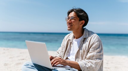 Fototapeta premium Young man working on laptop on a sunny beach with ocean background