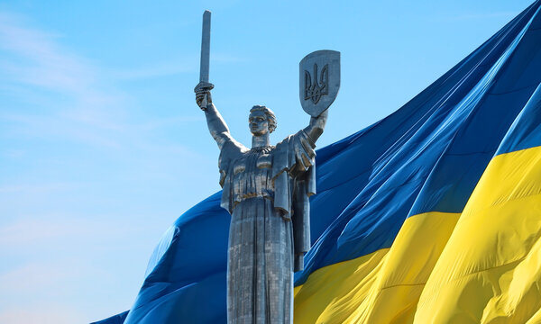 The Motherland Monument rises before a large Ukrainian flag, symbolizing national unity, resilience, independence, strength, and patriotism in Ukraine. Ukraine national sculpture.