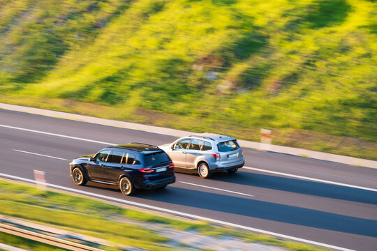 German Luxury SUV overtaking silver japanese car on asphalt highway road, road trip concept, blurred motion