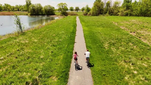 Aerial view of couple cycling paved path through nature with wildlife and water views, St Lawrence Parks, Ontario. Active lifestyle, healthy living, outdoor recreation, Canadian landscape.