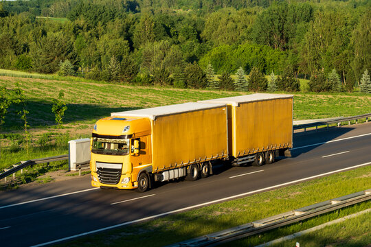 Yellow Road Train Truck Driving on Highway Through Green Countryside, Concept of Long Distance Freight Transportation and Supply Chain Logistics