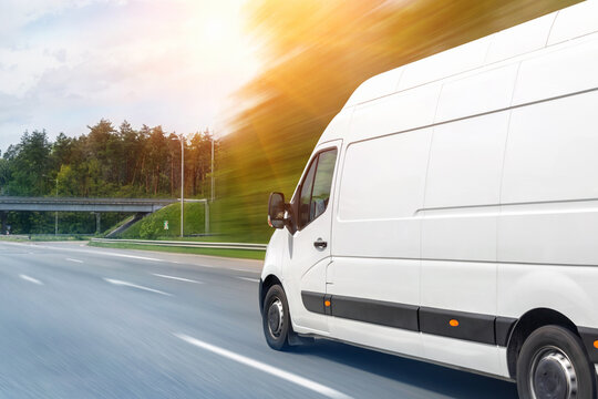 White modern delivery small shipment cargo courier van moving fast on motorway road to city urban suburb. Business distribution and logistics express service. Mini bus driving on highway on sunny day