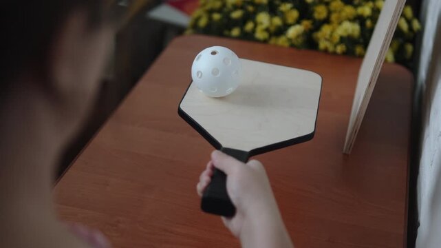 Unrecognizable caucasian man rolls pickleball ball over paddle. Over the shoulder view of home training session for ball control and developing agility in pickleball.