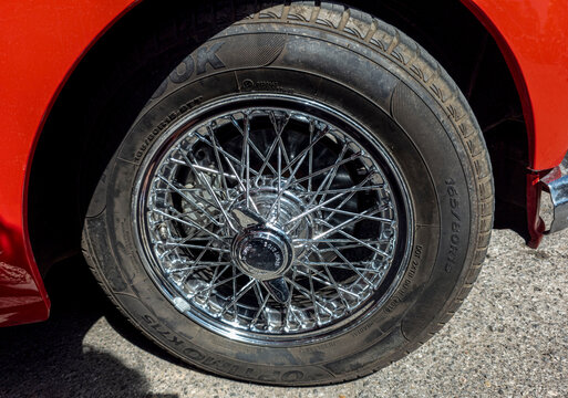 TAVERNES BLANQUES, SPAIN - JUNE 14, 2026.Close view of polished chrome wire wheel with vintage knock off spinner on classic red MG MGA convertible sports car