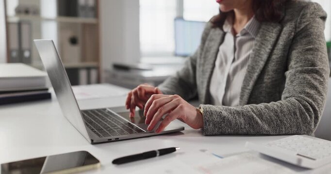 Woman accountant typing on laptop in office. She manages finance data and bookkeeping, entering numbers and preparing reports. Focus on accuracy, compliance, and business efficiency.