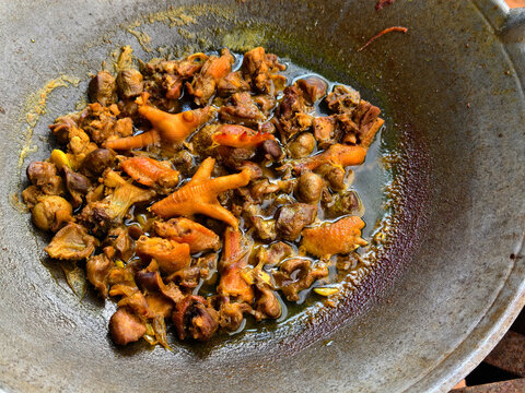 A close-up of chopped chicken including chicken feet being simmered and seasoned with soy sauce in a large metal wok. Traditional Asian cooking style, local cuisine, and food preparation.