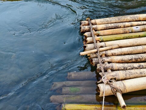 A top view of a traditional handmade bamboo raft tied with rope, floating on clear river water. Perfect for eco-tourism, outdoor adventure, tropical travel, and nature background concepts.