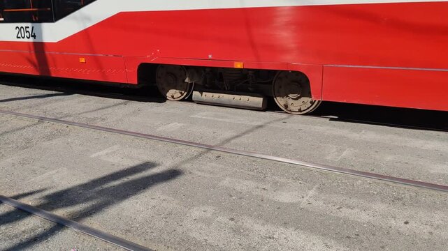 red and white tram moves left to right on rails with close-up view of wheels. modern public transport vehicle travels on urban tracks providing efficient city transportation.
