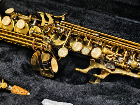 A detailed close-up shot of a polished golden brass saxophone lying in a soft black velvet case. Featuring intricate mechanism and mother-of-pearl buttons, perfect for music and musical instrument the
