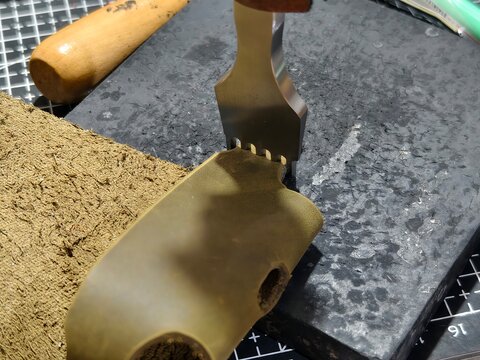 A detailed close-up of leather crafting process. A craftsman using a steel stitching punch tool on brown leather material, perfect for DIY, handmade workshop, and artisan concepts.