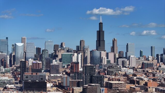 Aerial view of the Chicago skyline featuring the Willis Tower rising above dense urban architecture under a clear blue sky in Chicago, Illinois, United States.