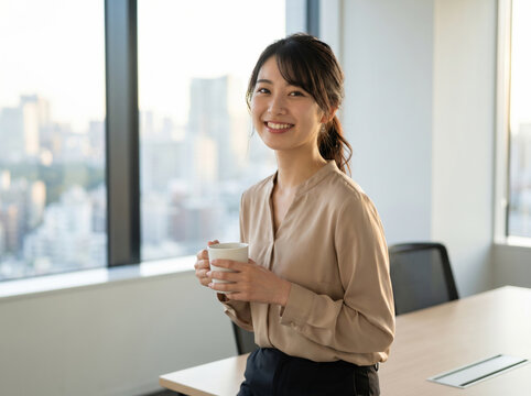夕方のオフィスでマグカップを両手で持ち微笑む女性