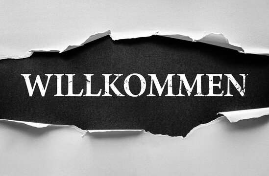 Torn paper effect revealing the German word WILLKOMMEN, meaning welcome, in bold distressed font. Concept of greeting, invitation, hospitality, arrival, cultural message, and friendly reception