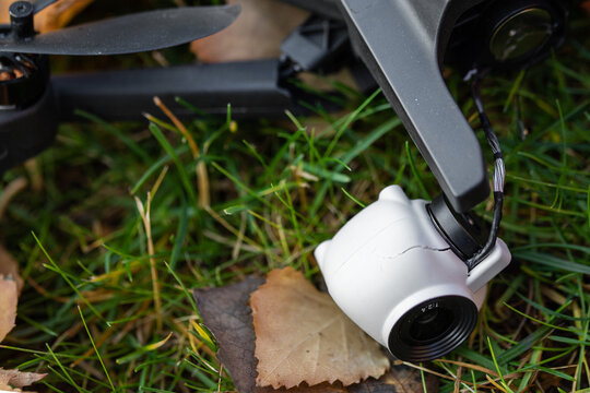 Broken black quadcopter drone uav lying on green grass lawn on ground after crash accident. Remote control failure due to strong wind interference. Cracked camera gimball and plastic legs