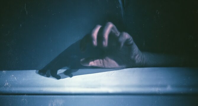 A pale hand emerges from darkness, fingers reaching, casting a stark shadow