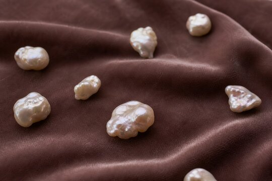 Irregular pearl nodules scattered on velvet fabric in close-up with soft texture and shallow depth.