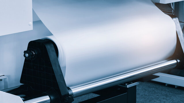 A large wide industrial CMYK printer prints a color image on fabric or paper.
