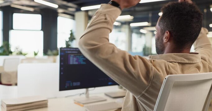 Developer programmer coding success celebration in office. Rear view of a confident software engineer raising arms after fixing errors at a computer monitor. Clear concept of success at work.