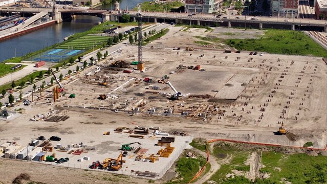Aerial view of a large construction site featuring heavy machinery, cranes, and foundation work in progress near a river and bridge in Chicago, Illinois, United States.