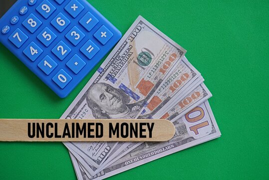 Wooden piece written UNCLAIMED MONEY. Financial concept. Account freeze problem management. Unclaimed property. US Dollar and calculator background