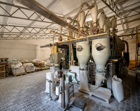 Automated flour bagging and weighing station featuring large cyclone funnels industrial scales and white packaging sacks inside a large local agricultural grain processing factory workshop