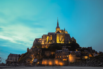 Naklejka premium Evening view of the historic tidal island of Mont Saint-Michel illuminated against a twilight sky in Normandy