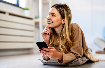 Fototapeta premium Smiling young woman chatting in social networks, working, using mobile applications at home.
