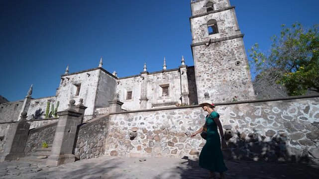 A senior woman smiles and walks alongside the historic San Javier Mission in Baja California Sur during sunrise, enjoying her adventure
