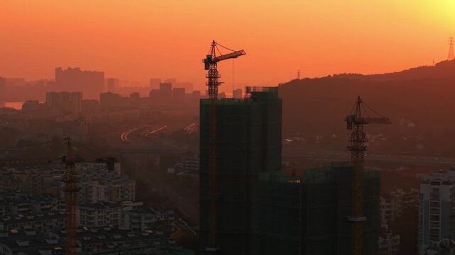 Orange sky over construction site during sunset, buildings under construction with cranes in the evening