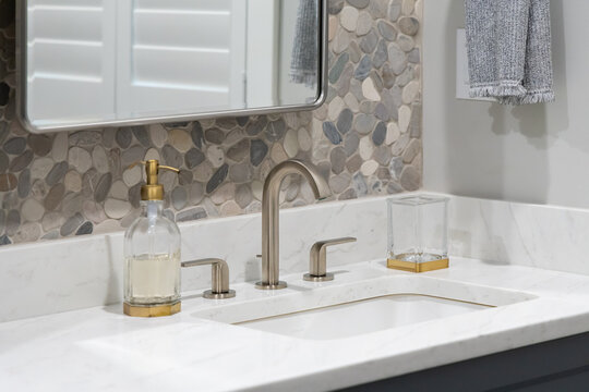 A bathroom faucet detail with blue cabinets, a stone tile backsplash, bronze faucet, and decor on the marble countertop.