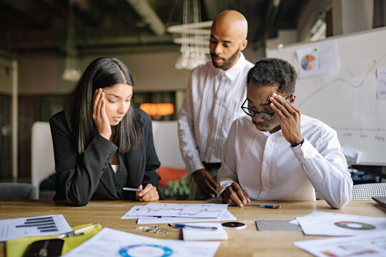 A diverse team reviews financial data with a boss explaining errors leading to significant losses. Two subordinates show distress, realizing their past actions caused financial downturns