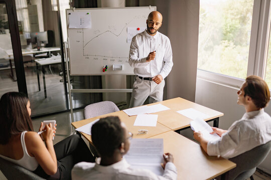 A speaker discusses investment strategies and market trends with attendees in a modern office setting, highlighting key data on a whiteboard for effective learning