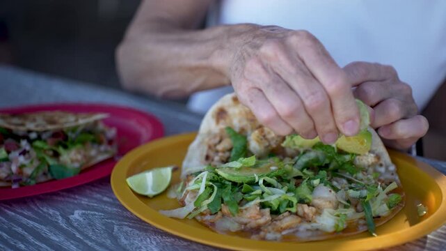 Senior woman enjoys squeezing lime on her fish and shrimp tacos in a local taco stand in Baja California.