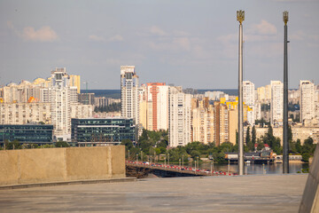 Naklejka premium Kyiv, Ukraine, panoramic cityscape a river bridge crossing the Dnipro River, with a vast skyline of residential areas and high-rise buildings on the left bank, adorned with national symbols