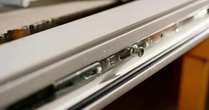 Close-up tracking shot along the metallic locking hardware installed inside a white window profile