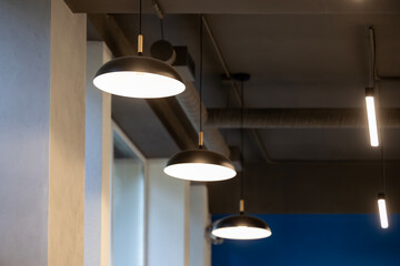 Obraz premium Multiple modern pendant light fixtures and a linear light strip illuminate a contemporary indoor space with architectural columns, textured walls, and a dark ceiling, providing ambient lighting for th